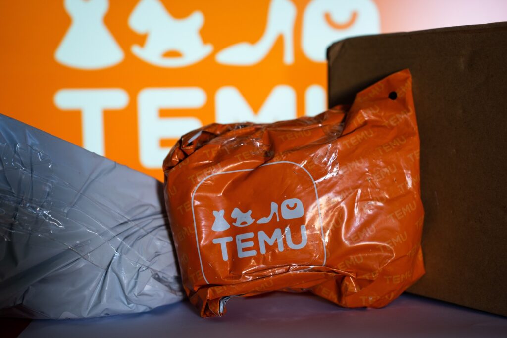 A package from Temu among with other packages, in front of a screen with the logo of Temu. Temu Marketplace
