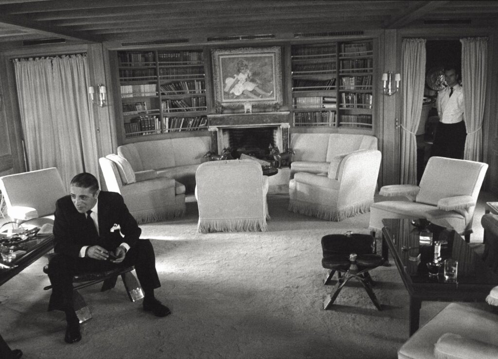 Poslovnež Aristotel Onassis na jahti med intervjujem v dnevni sobi s kaminom, nad katerem je izobešena Renoirova slika otroka v travi